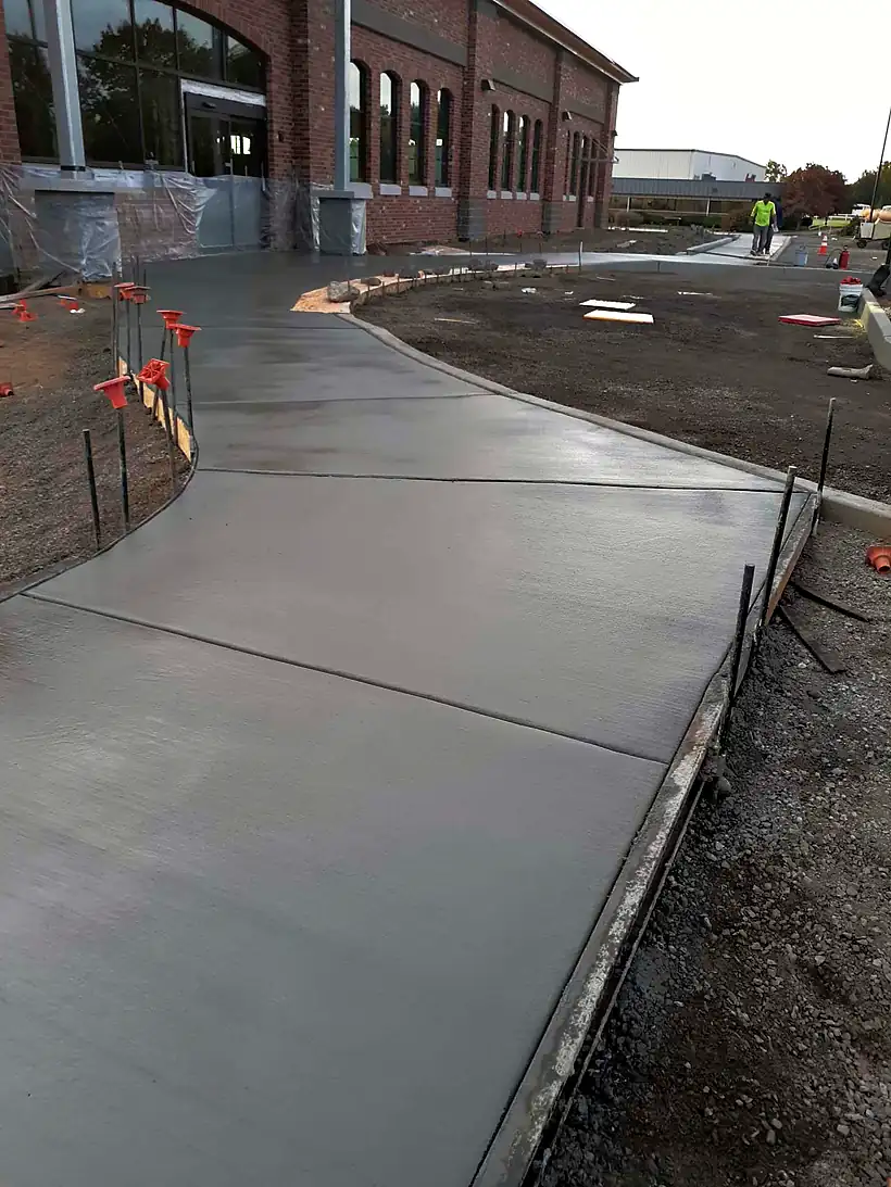 Freshly finished concrete driveway by Reyes Brothers Construction, running alongside a brick building